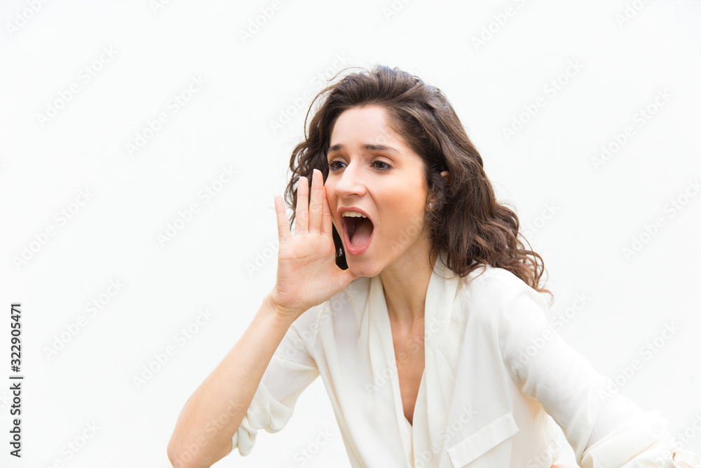 Beautiful young woman screaming. Attractive young lady holding hand near open mouth. Attention concept Beautiful young woman screaming. Attractive young lady holding hand near open mouth. Attention concept
