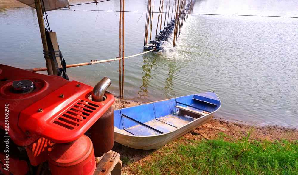 Selective focus at orange motor engine on foreground with blurred blue boat and aerator multiple turbine wheels on water surface for increase oxygen in shrimp pond and natural farm background Selective focus at orange motor engine on foreground with blurred blue boat and aerator multiple turbine wheels on water surface for increase oxygen in shrimp pond and natural farm background