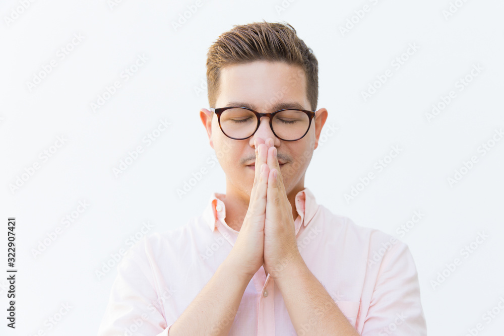 Handsome serene young man praying. Young guy with hands together in praying gesture and closed eyes. Hope and please concept Handsome serene young man praying. Young guy with hands together in praying gesture and closed eyes. Hope and please concept