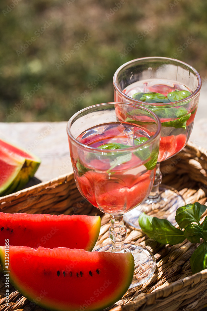 On a table in the garden in a basket are two glasses of lemonade and sliced of watermelon On a table in the garden in a basket are two glasses of lemonade and sliced of watermelon
