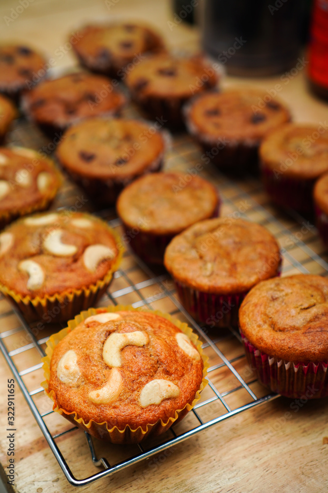A lot of banana cupcakes on a cooling rack, some pieces have cashew nut or chocolate chip that on the wooden table A lot of banana cupcakes on a cooling rack, some pieces have cashew nut or chocolate chip that on the wooden table