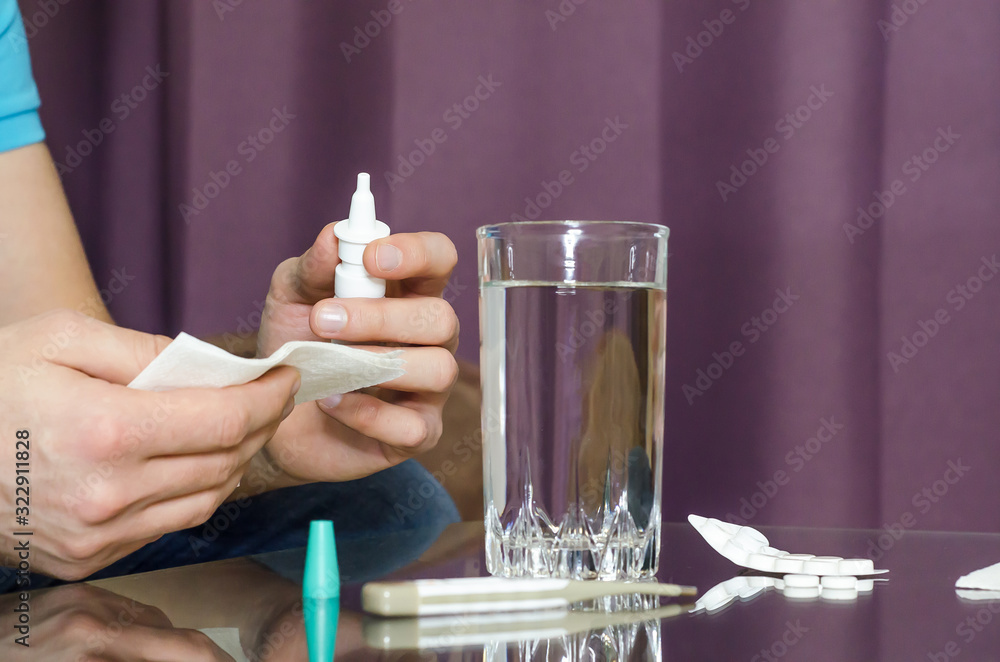 Fototapeta premium sick man sprays drops in his nose, blows in napkin, takes medicine, pills, measures the temperature, drinks water, close up. Health care.