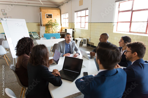 Confident leader talking to subordinates. Concentrated workers sitting at table and listening boss. Business meeting concept