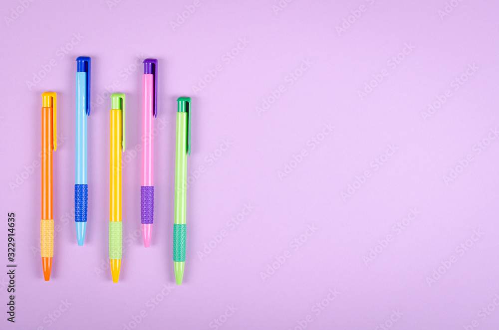 Fototapeta premium Different colored pens, school ballpoint on purple background composition.