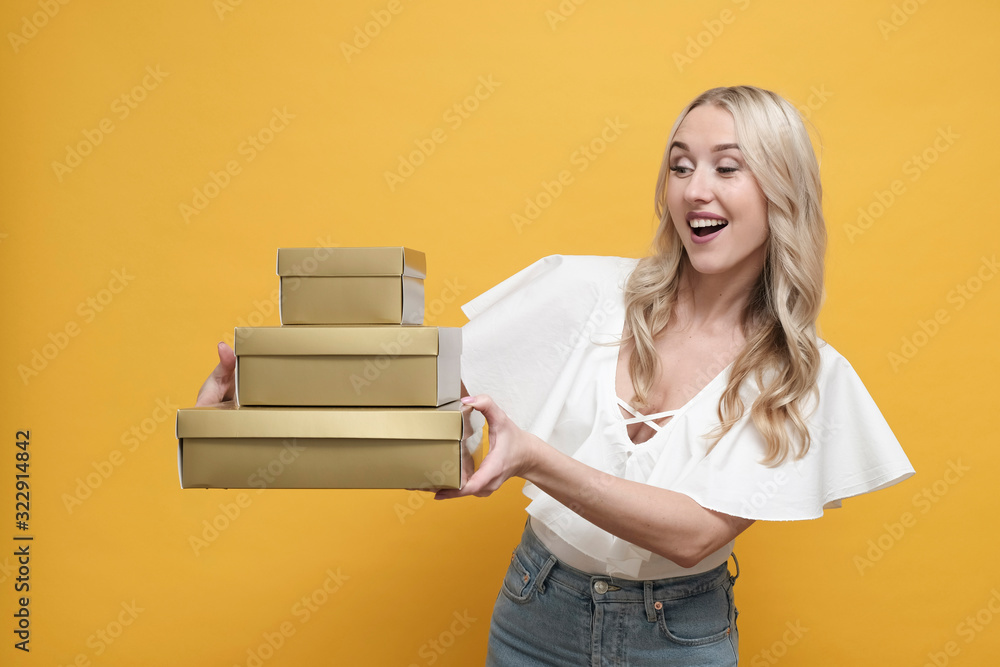 Happy blond european woman in white blouse holding a pack of gift boxes over yellow background. Copy space Happy blond european woman in white blouse holding a pack of gift boxes over yellow background. Copy space