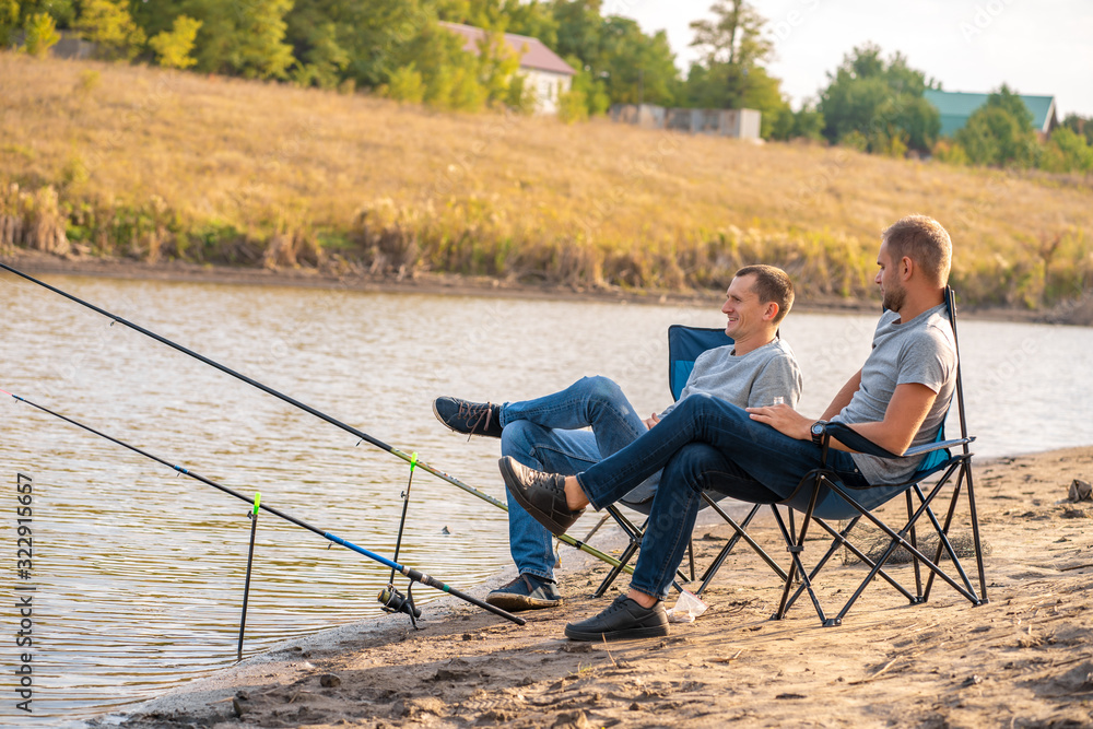leisure and people concept. Happy friends with fishing rods on pier by lakeside. leisure and people concept. Happy friends with fishing rods on pier by lakeside.