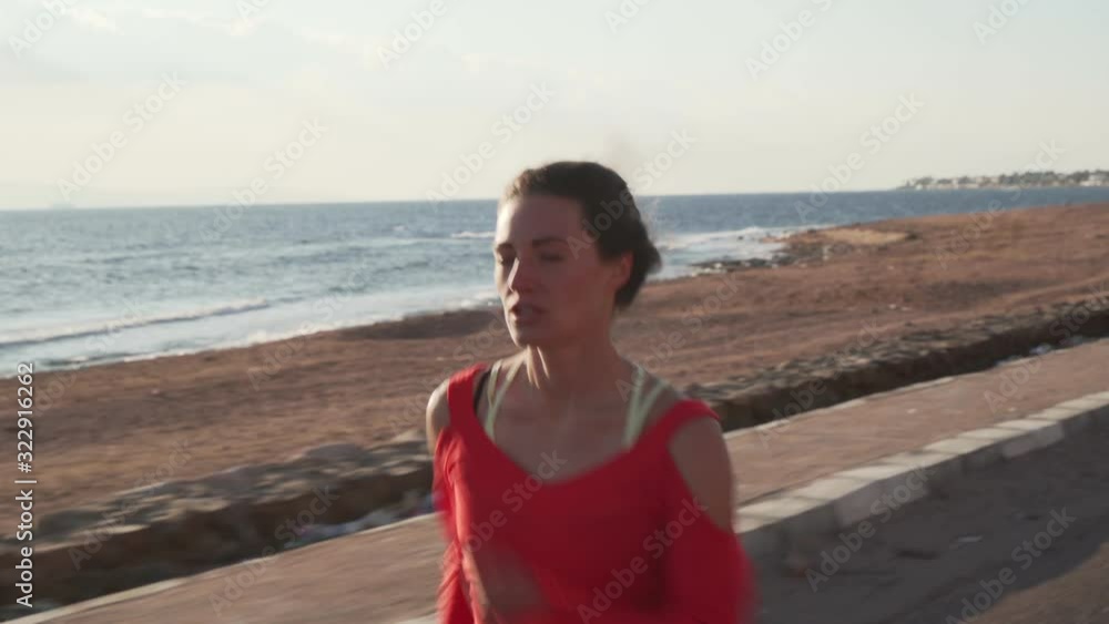 Athletic woman in sportswear running on promenade at sunset near ocean Athletic woman in sportswear running on promenade at sunset near ocean