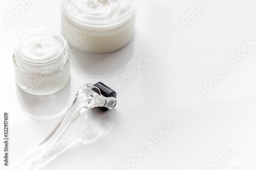 Dermaroller for home cosmetologic procedure near creams on white background copy space