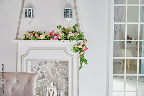 A white fireplace with red flowers and a glass door with wooden slats in a room with light walls. Background for a photo shoot in a Studio