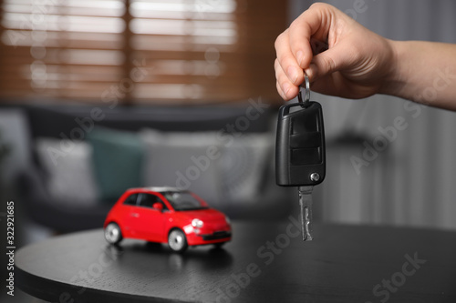 Man holding key near table with miniature automobile model indoors, closeup. Car buying
