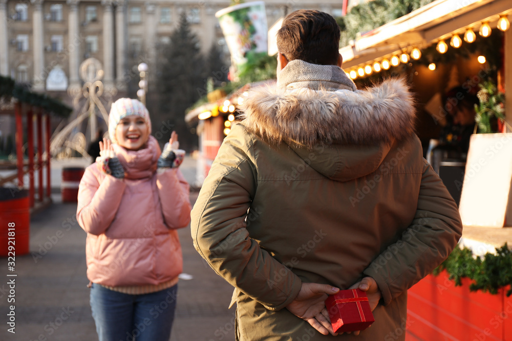 Man presenting Christmas gift to his girlfriend at winter fair Man presenting Christmas gift to his girlfriend at winter fair