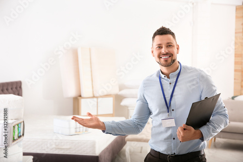 Happy salesman with clipboard in mattress store. Space for text