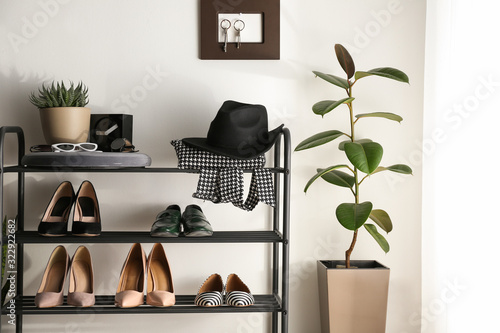 Black shelving unit with shoes and different accessories near white wall in hall © New Africa