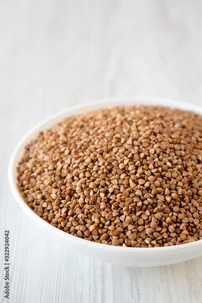 Uncooked Roasted Buckwheat in a white bowl on a white wooden background, side view. Copy space. Uncooked Roasted Buckwheat in a white bowl on a white wooden background, side view. Copy space.