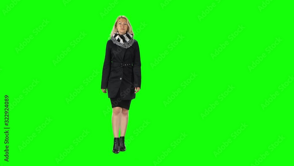 Blonde girl in a black dress, coat, scarf and boots going against a green screen. Blonde girl in a black dress, coat, scarf and boots going against a green screen.