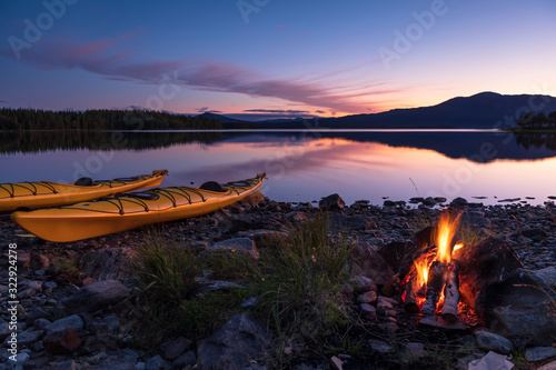 Fototapeta Naklejka Na Ścianę i Meble -  Campfire during dusk at the shore of a lake with two kayaks. Sweden.