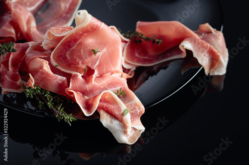 Prosciutto with thyme on a black plate.