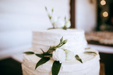 White wedding cake decorated with white roses and green branches with leaves
