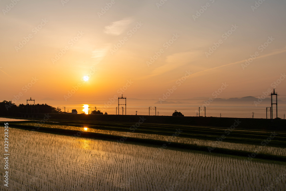 オレンジ色の日の出と水田と琵琶湖と線路
