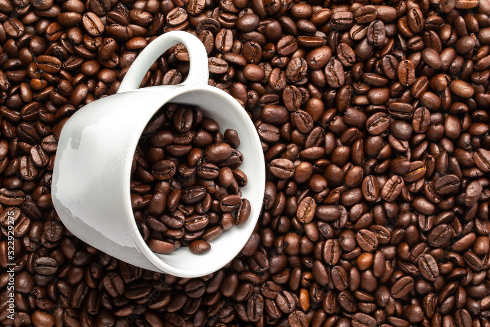 White cup with coffee beans on a background of coffee beans White cup with coffee beans on a background of coffee beans