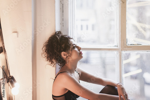 sad girl sitting on the windowsill and looking out the window