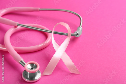 Pink ribbon and stethoscope on color background, closeup. Breast cancer concept