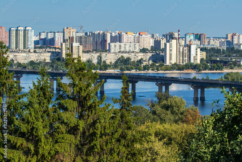 View of the Dnieper, the Paton Bridge and the Left Bank of Kyiv on a sunny day. Skyline of Kyiv. Nature and cityscape together in ukrainian capital. Ukraine.