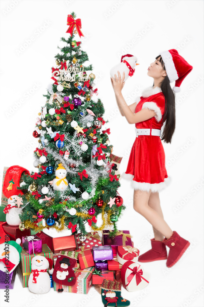 Pretty girl wearing santa costumes standing by christmas tree on white background. Pretty girl wearing santa costumes standing by christmas tree on white background.