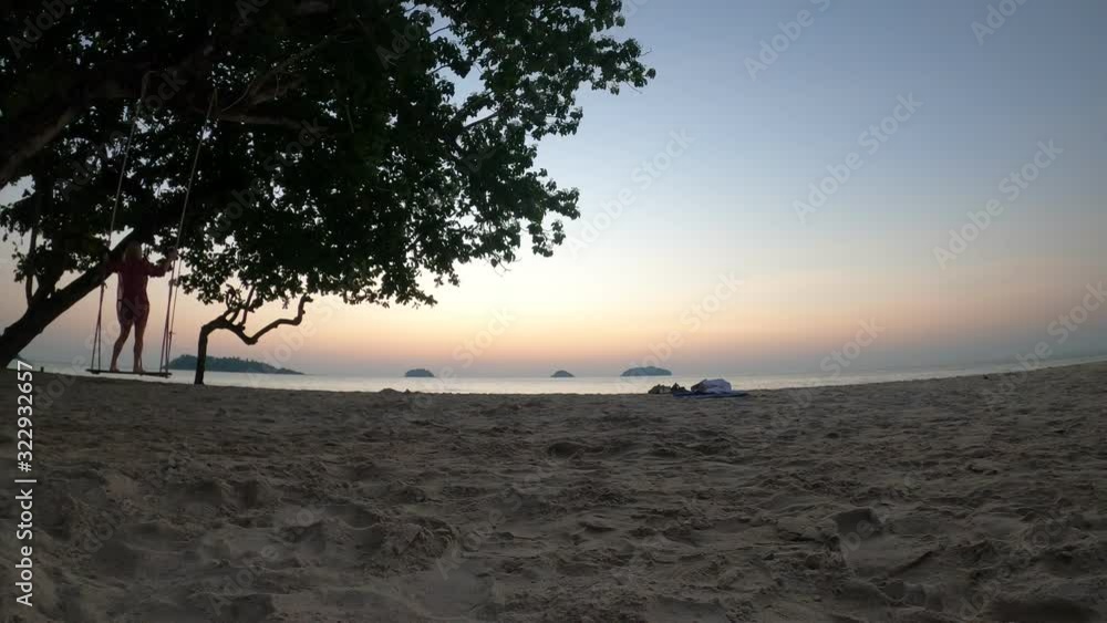 Time lapse of sunset at a tropical island, view from the beach at the sea, people are swinging on a swing from a tree. Time lapse of sunset at a tropical island, view from the beach at the sea, people are swinging on a swing from a tree.