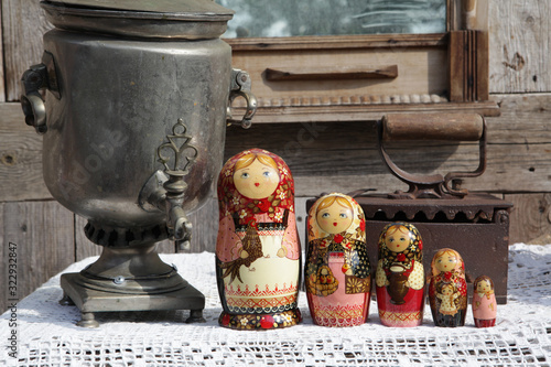 Russian traditional wooden nested dolls, matryoshka, in form of women in national costumes. Ancient iron, antique silver samovar for tea drinking. Russian style in folk art, handicraft, ethnic craft photo