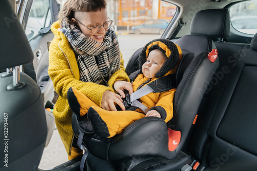 Car Seat for children with security system. A woman with a smile fastens seat belts to her child’s chair. © galaganov