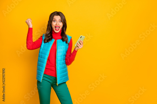 Portrait of ecstatic cheerful girl use smartphone search social media news win online lottery raise fists scream yes wear red blue green pants trousers isolated over bright color background