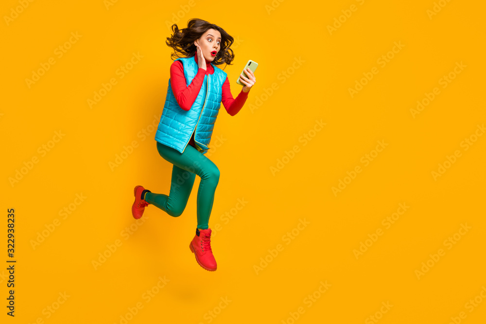 Full length profile side photo astonished girl jump use smartphone read unbelievable social network information run wear red blue green vest pants boots isolated bright shine color background