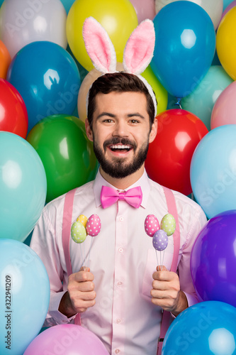 Happy easter. Vertical photo of funny guy colorful decor party festive mood hold eggs sticks wear pink shirt bow tie suspenders fluffy bunny ears on balloons creative background