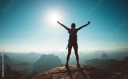 Cheering woman backpacker enjoy the view on sunrise mountain top cliff edge photo