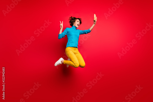 Full length photo of crazy funky bob brunette hair girl jump enjoy spring fall holiday make selfie v-sign smartphone blogging wear blue sweater yellow outfit isolated bright red color background