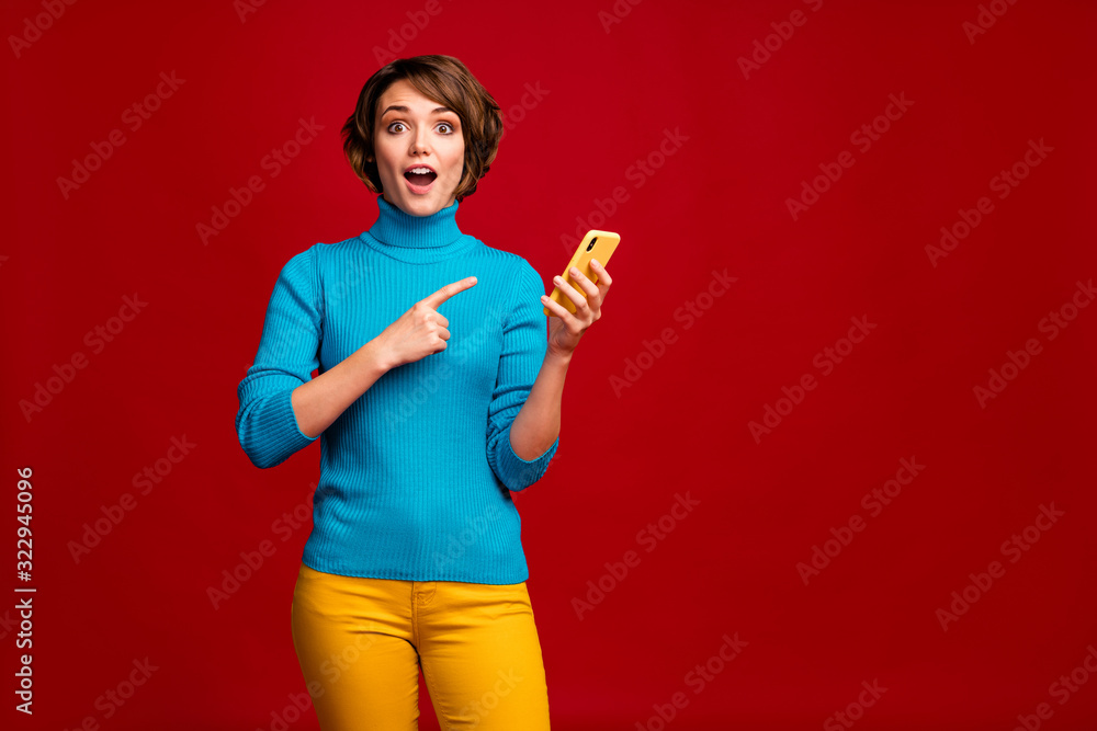 Portrait of crazy girl use smartphone search social media news read sales  discount point index finger device scream wow omg wear yellow shine blue  clothes isolated red color background foto de Stock
