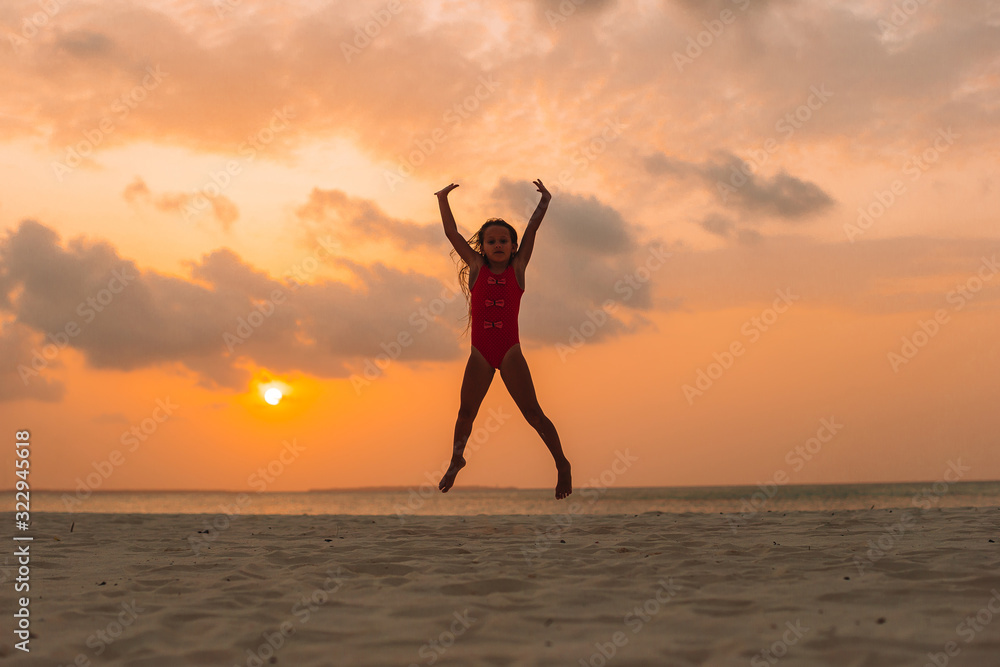 Adorable happy little girl on white beach at sunset.