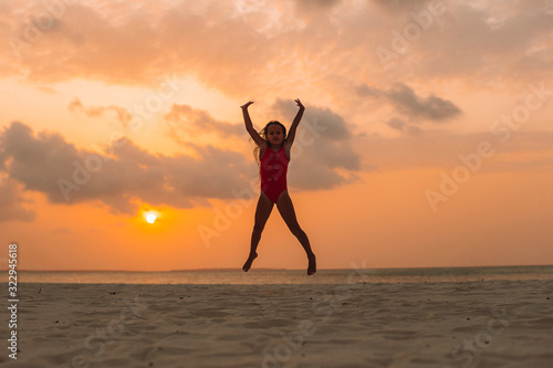 Adorable happy little girl on white beach at sunset. © travnikovstudio
