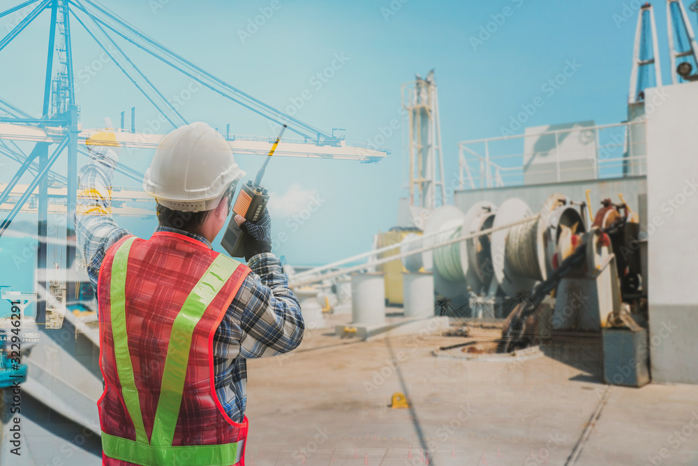 Engineer, Pilot captain with walkies talkie in hand on vessel forward ship with anchor rope in drum and crane in port background