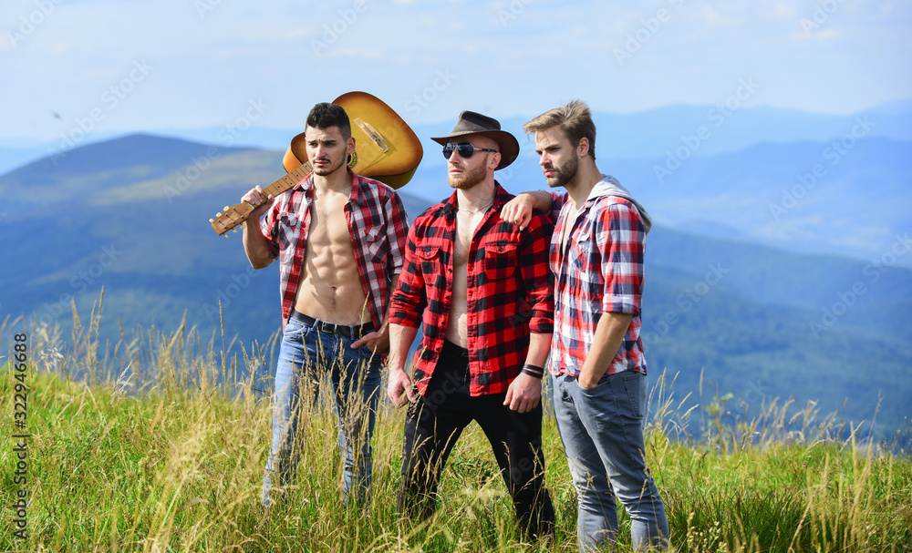 Long route. Tourists hiking concept. Hiking with friends. Men with guitar hiking on sunny day. Group of young people in checkered shirts walking together on top of mountain. Adventurers squad
