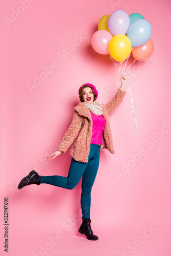 Full body vertical photo of funny model lady hold many colorful balloons flying up air open mouth wear modern fur coat scarf beret cap pants shoes isolated pink color background