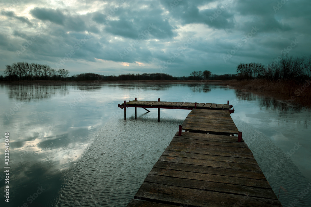 Fototapeta premium Drewniany most na jeziorze, deszczowe chmury na wieczornym niebie