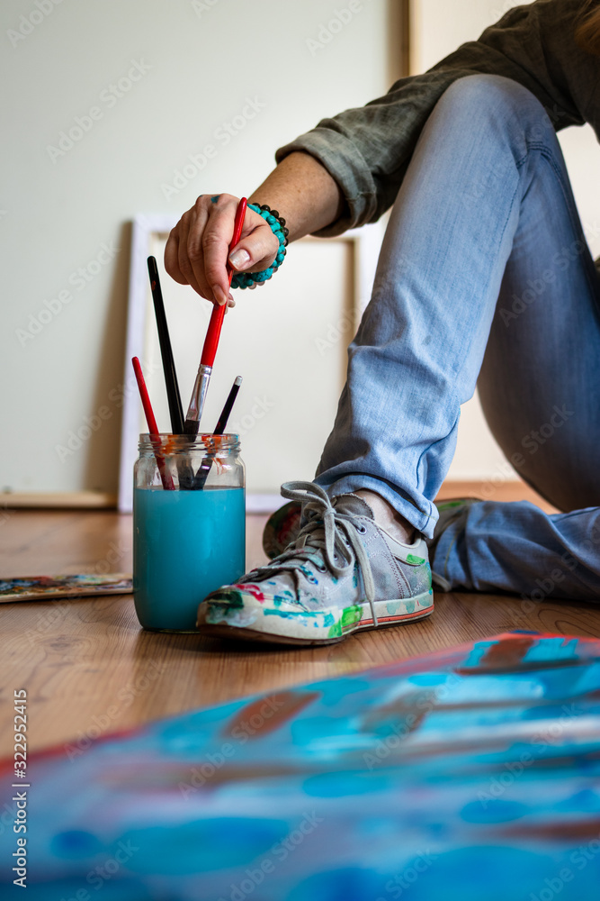 Artist woman holding paintbrush and sitting on floor after finished her abstract paintings