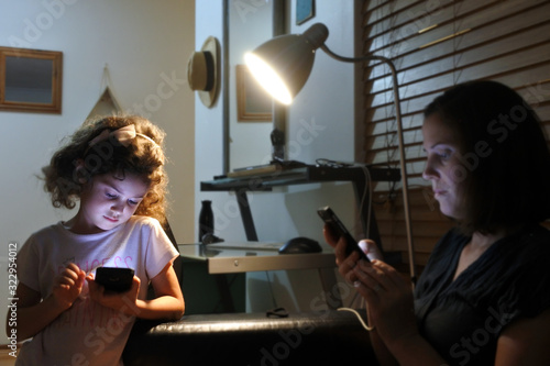 Young girl and mother reading messages on cellphone in home at night