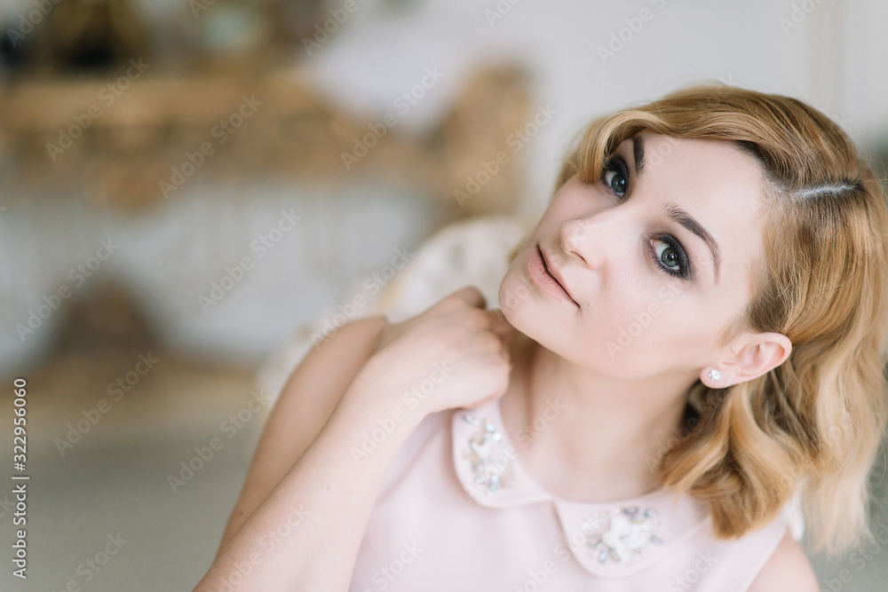 Beautiful young blonde woman in a pink dress smiles in a bright room in the morning. Beautiful young blonde woman in a pink dress smiles in a bright room in the morning.