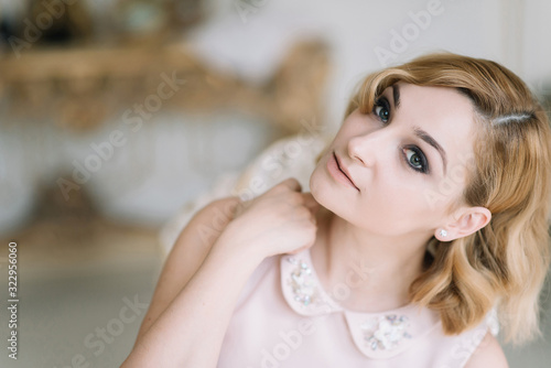 Beautiful young blonde woman in a pink dress smiles in a bright room in the morning.