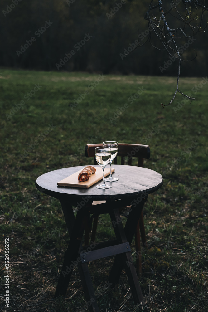 Spring picnic on nature – white wine in glasses and grill bread on wooden round table