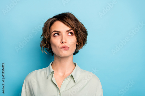 Closeup photo of attractive lady short hairdo wondered look up empty space biting lips pensive ponder wear casual green shirt isolated blue color background