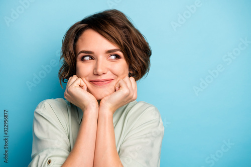 Closeup photo of attractive lady short hairdo arms hold chin head smiling overjoyed look side empty space wear casual green shirt isolated blue color background © deagreez